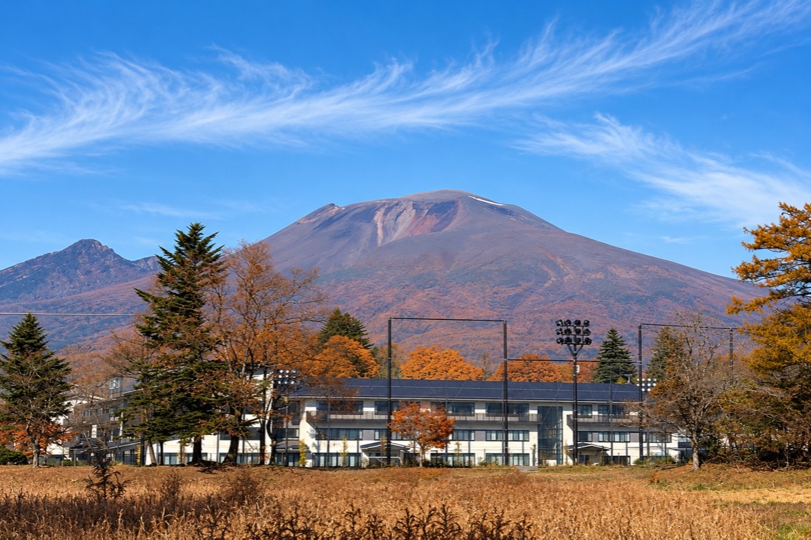 青空の下、紅葉した木々と建物の向こうにそびえる秋の浅間山